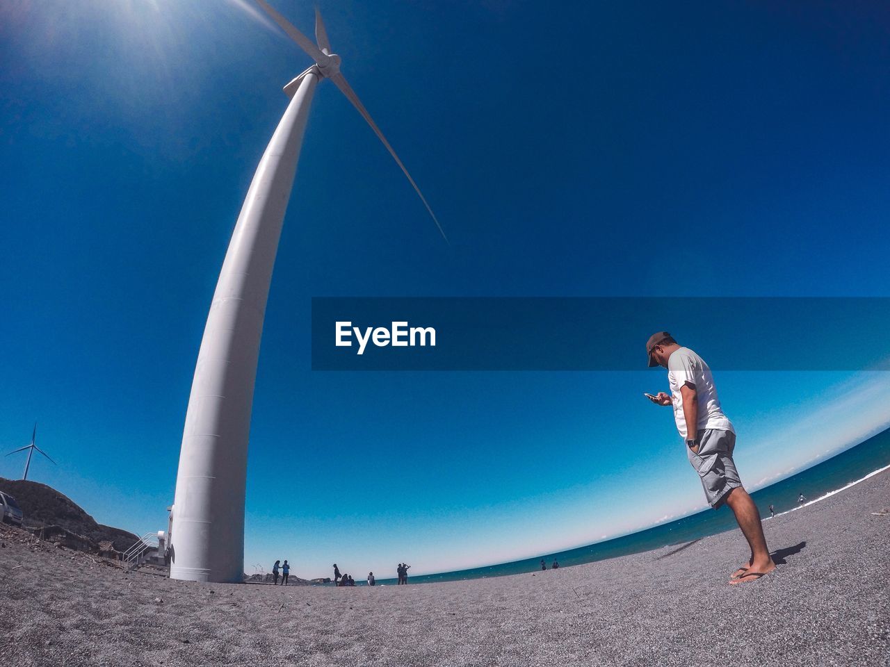 Low angle view of man standing by windmill against clear blue sky