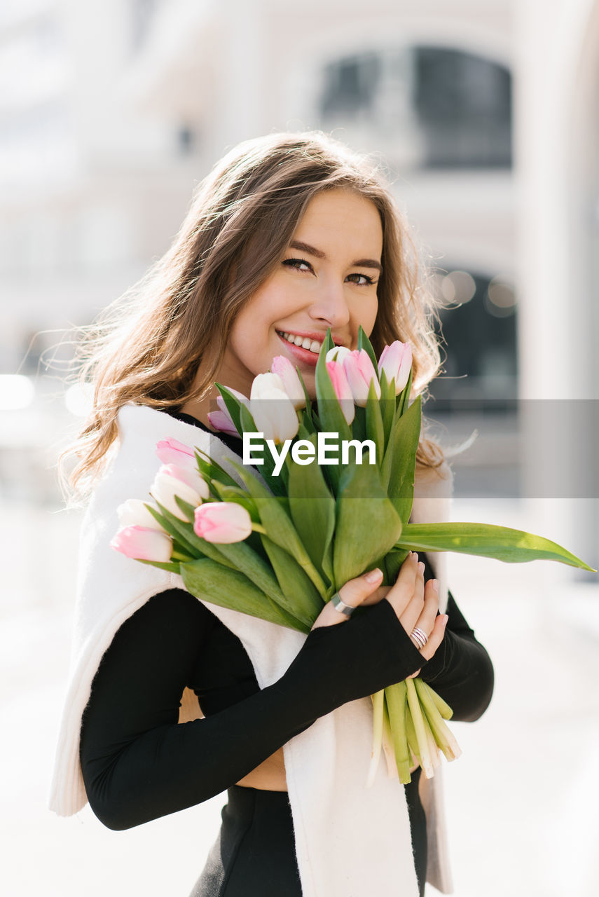 Smiling young woman with a bouquet of spring tulips on a city street