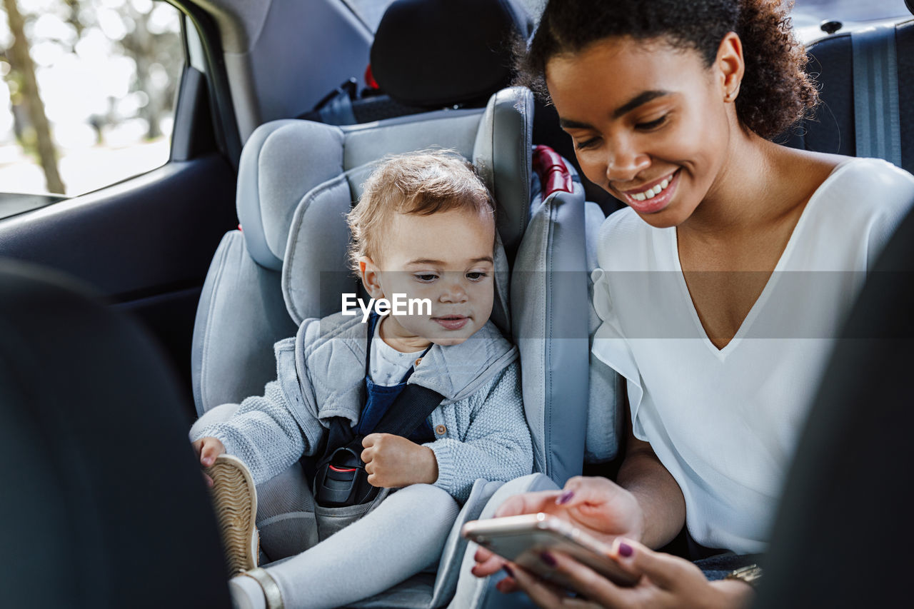 Mother with daughter while hold holding smart phone sitting in car