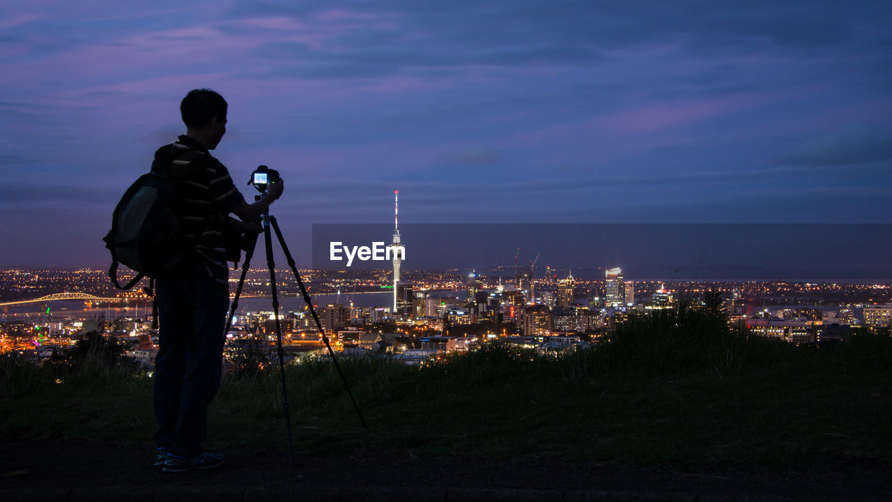 Rear view of man photographing cityscape against sky at night