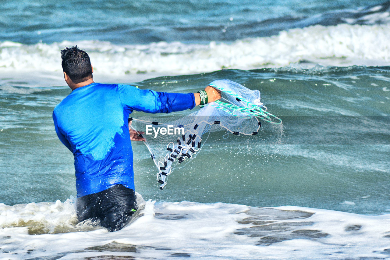 Rear view of man casting is fishing net at sea