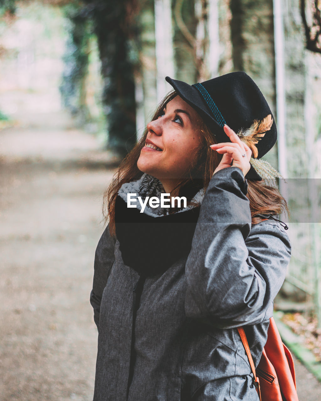 Smiling young woman looking up while wearing hat at public park