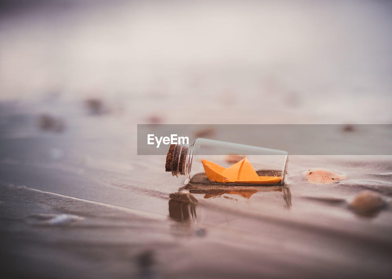 Miniature origami ship in bottle standing on sand at sunrise