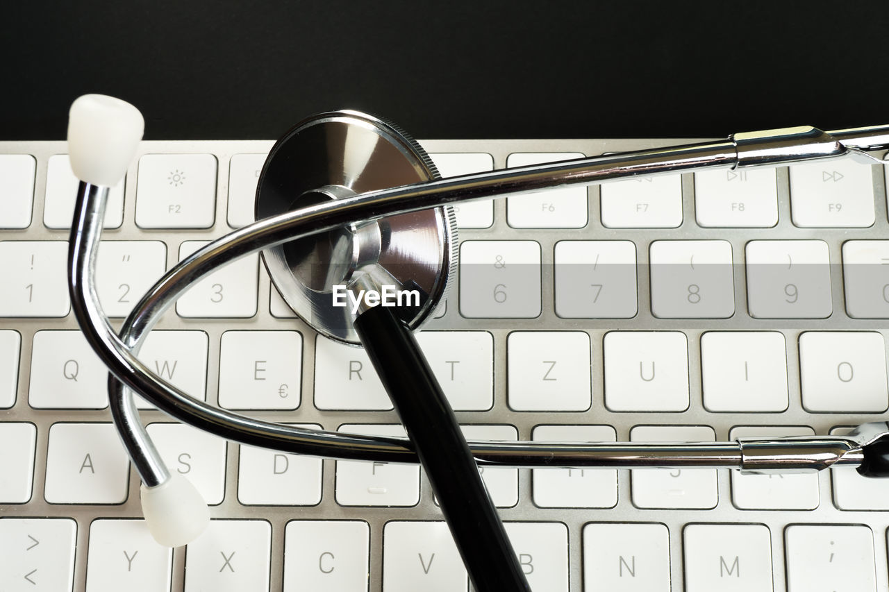 Directly above shot of stethoscope and computer keyboard against black background