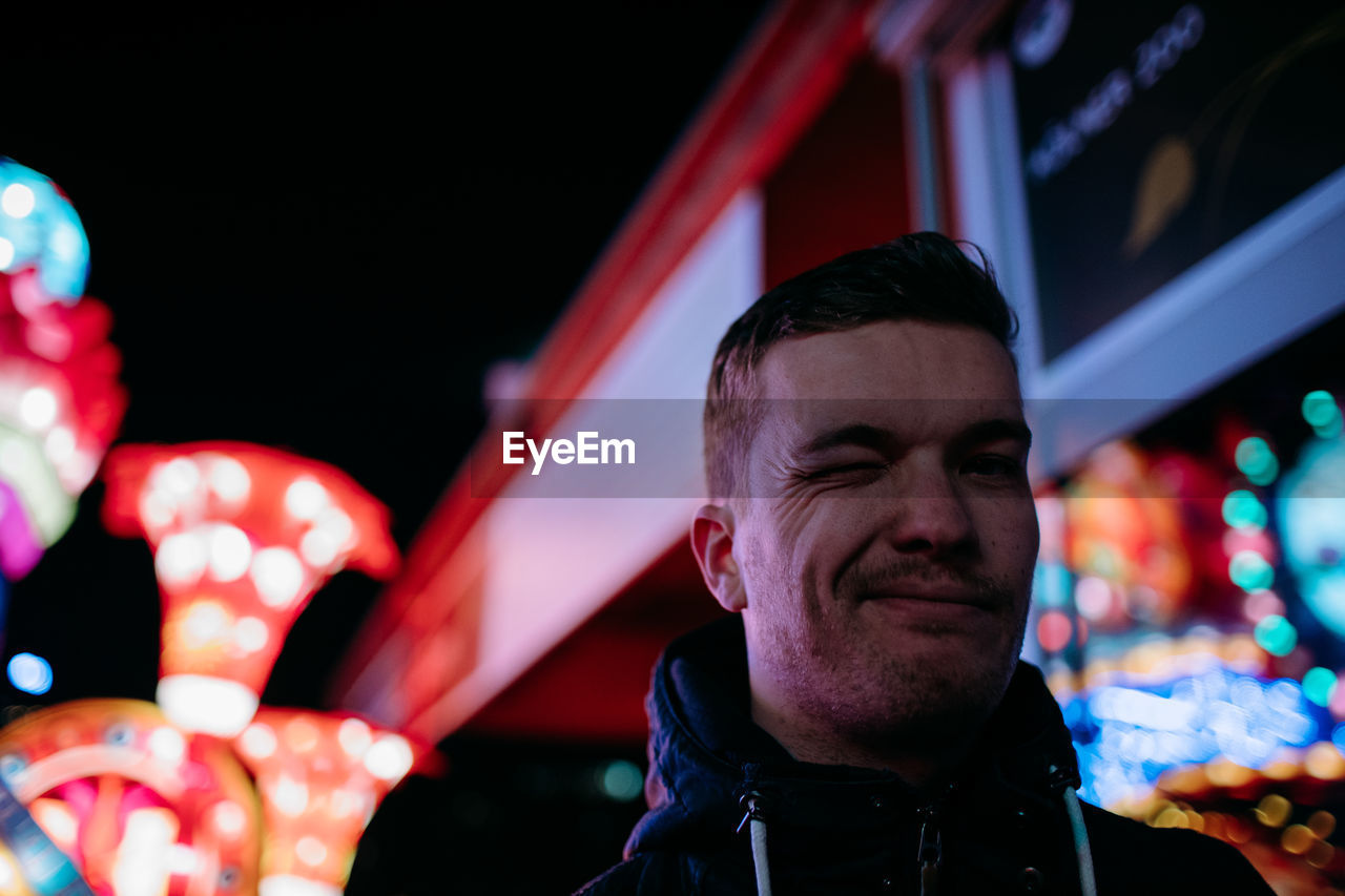 Low angle portrait of young man winking eye at amusement park