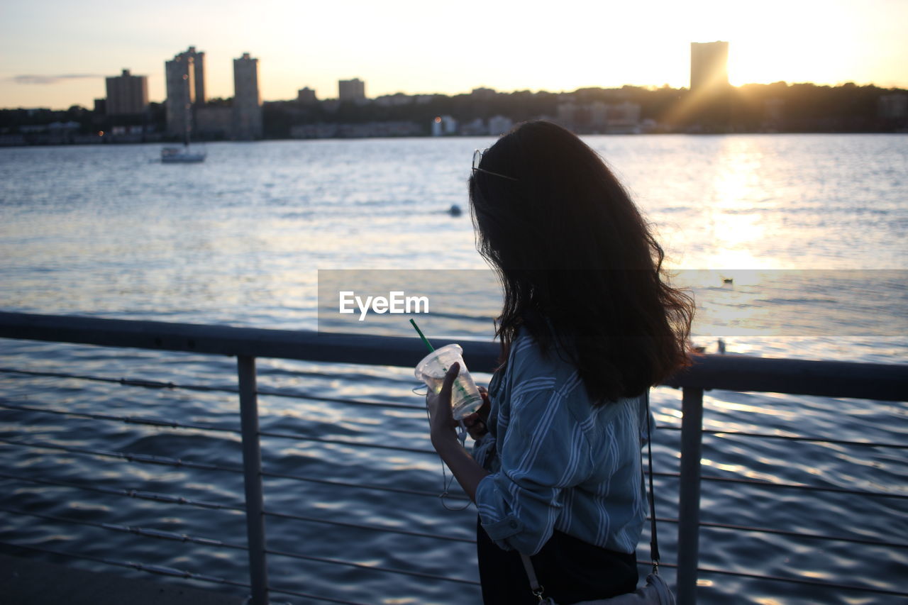 WOMAN STANDING ON RAILING IN SEA AGAINST CITY