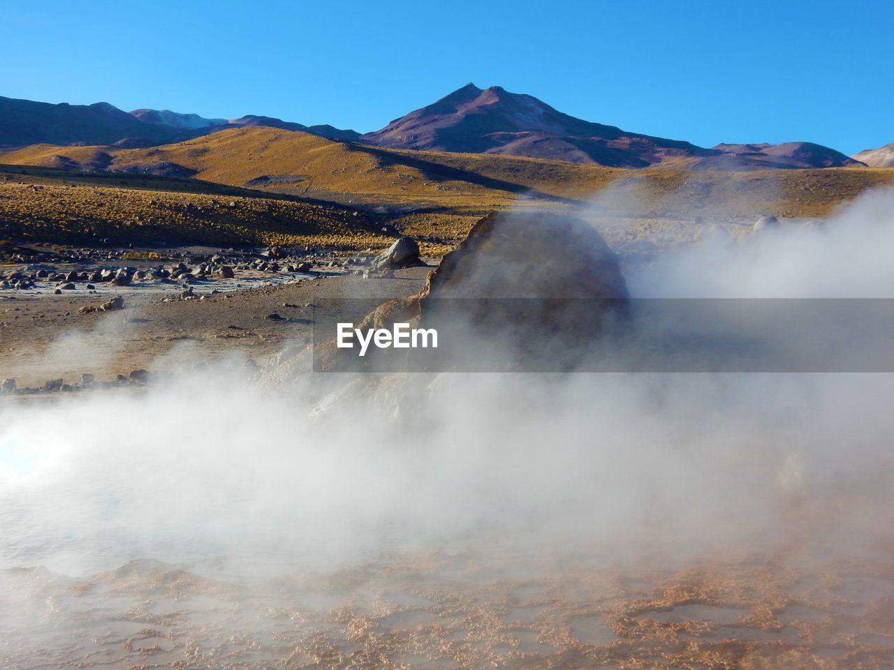 Smoke emitting from hot spring geyser against clear sky