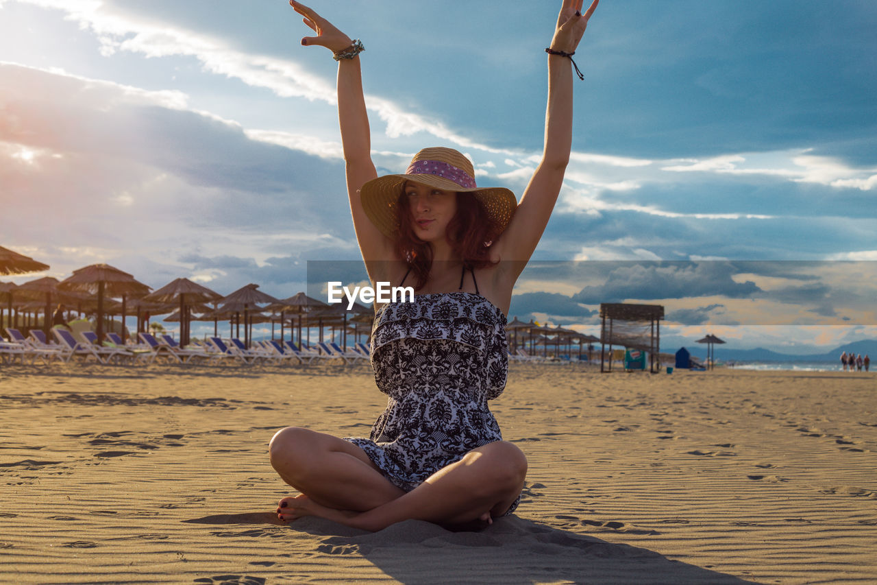 Full length of woman sitting on beach against sky