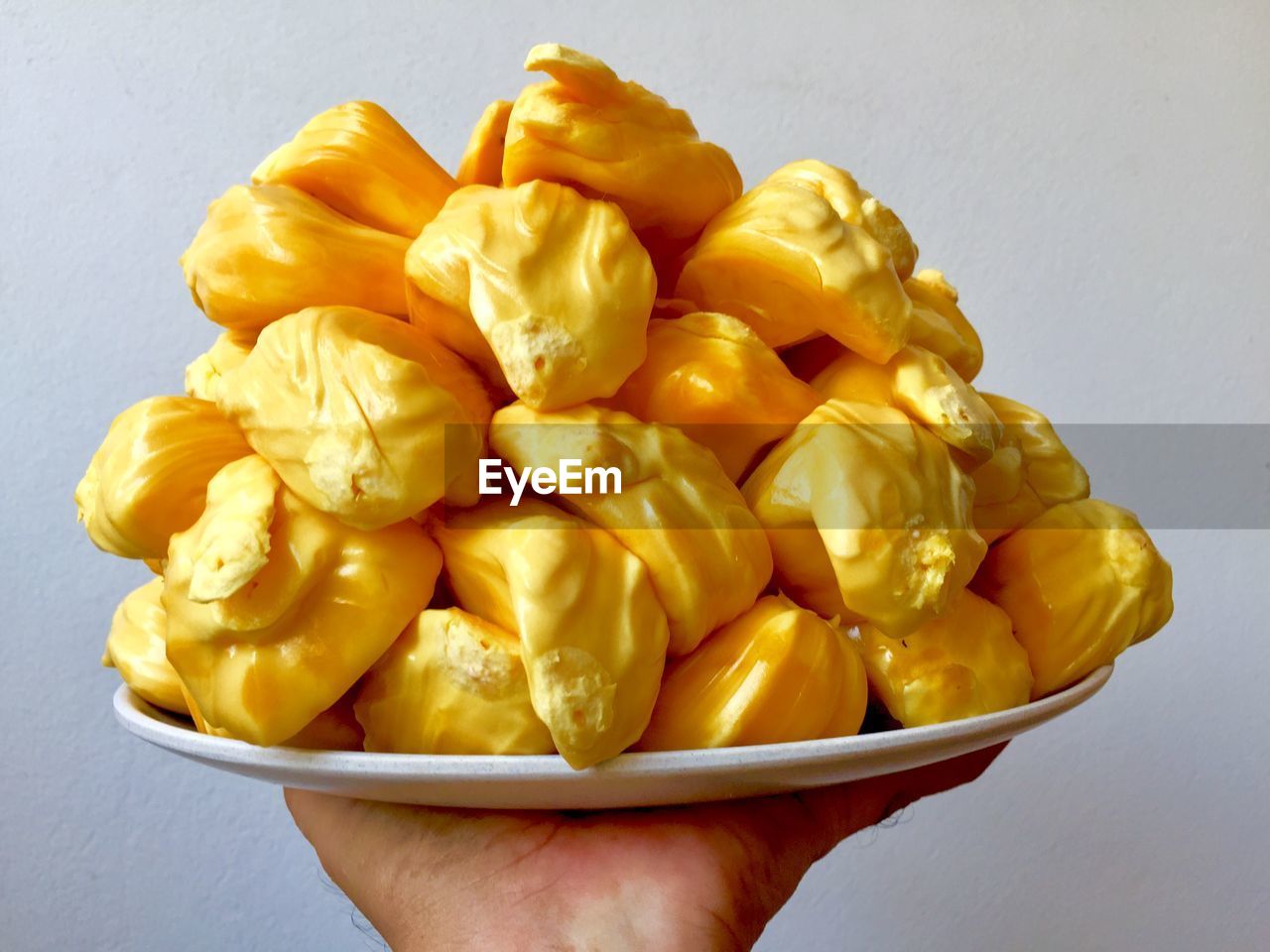 CLOSE-UP OF HAND HOLDING BOWL OF YELLOW AND VEGETABLE