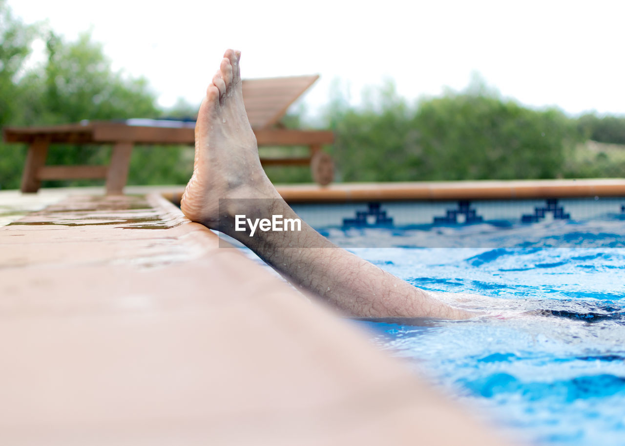 Low section of man swimming in pool against sky