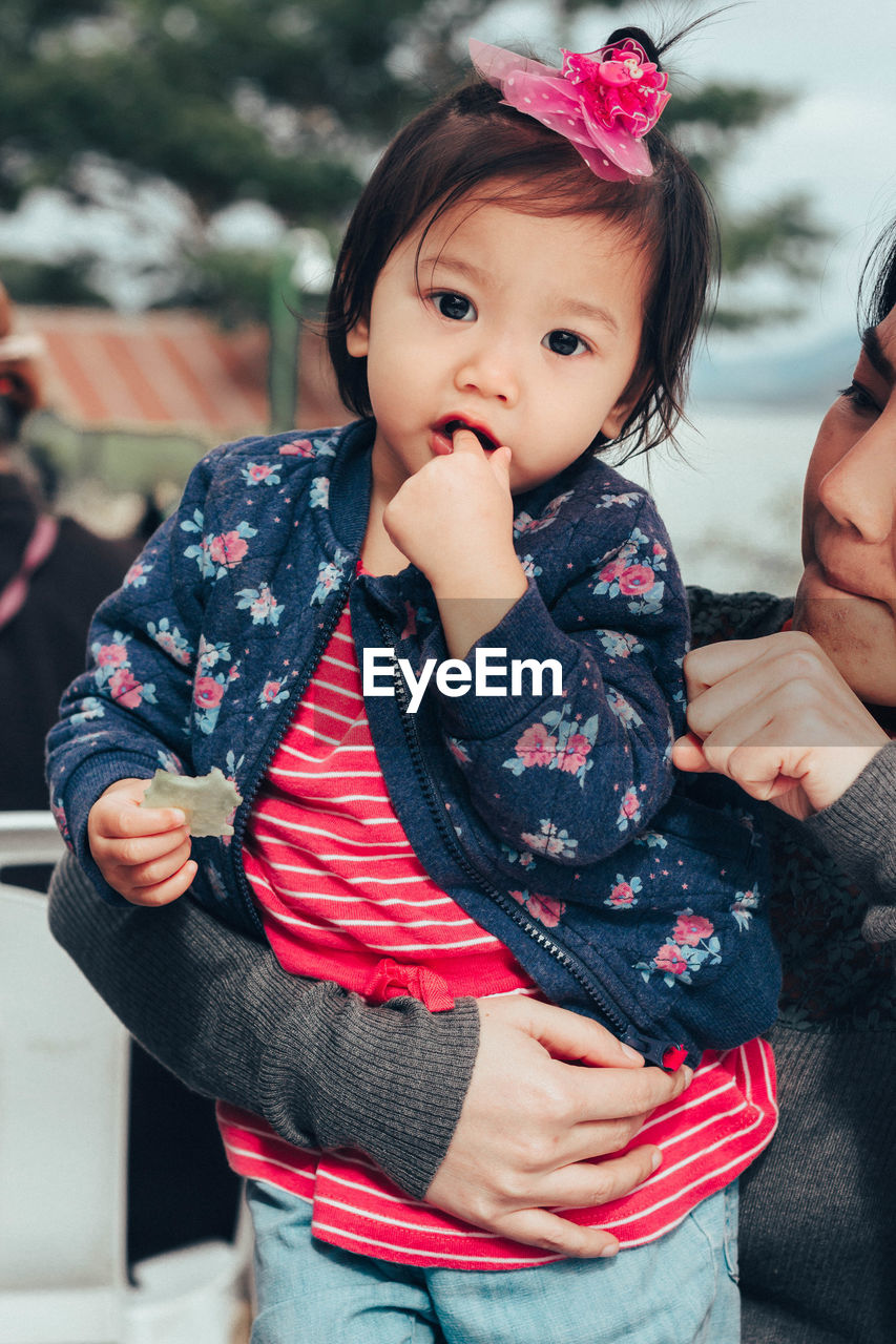Portrait of cute baby girl with mother standing outdoors
