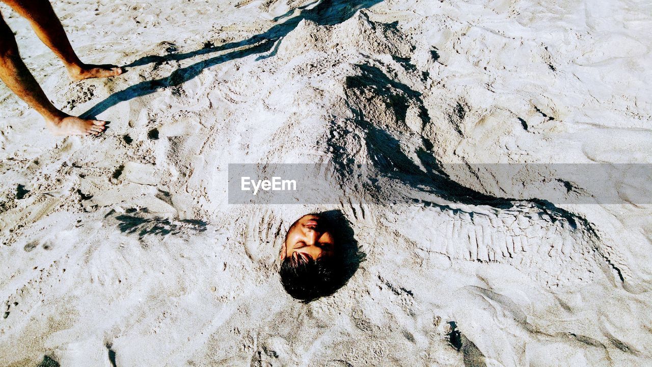 Low section of man with friend buried in sand