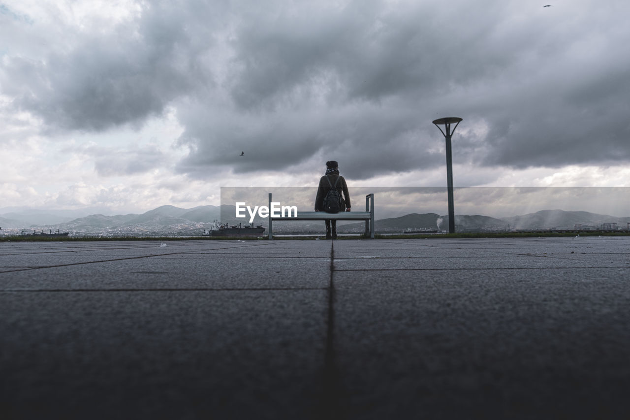 MAN ON STREET AGAINST CLOUDY SKY