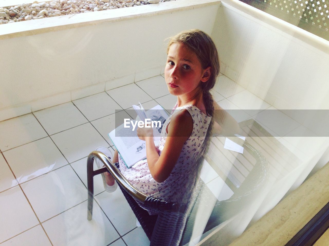 High angle portrait of cute girl reading book while sitting on balcony at home