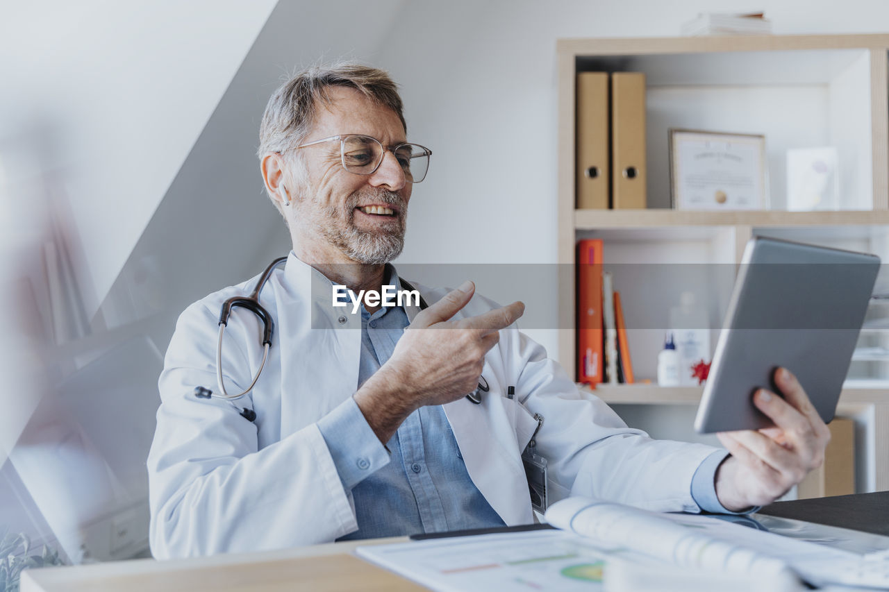 Smiling doctor talking on video call over digital tablet while sitting at clinic