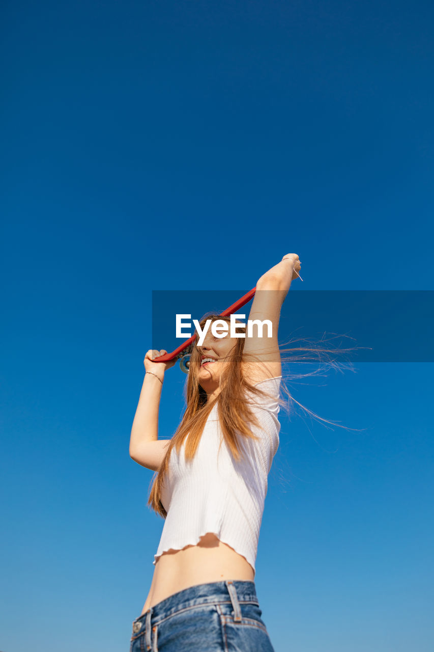 Happy teenage girl holding a skateboard over her head