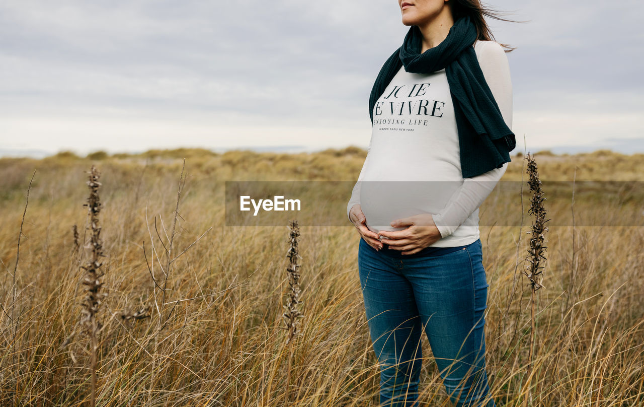 Midsection of pregnant woman standing on field against sky
