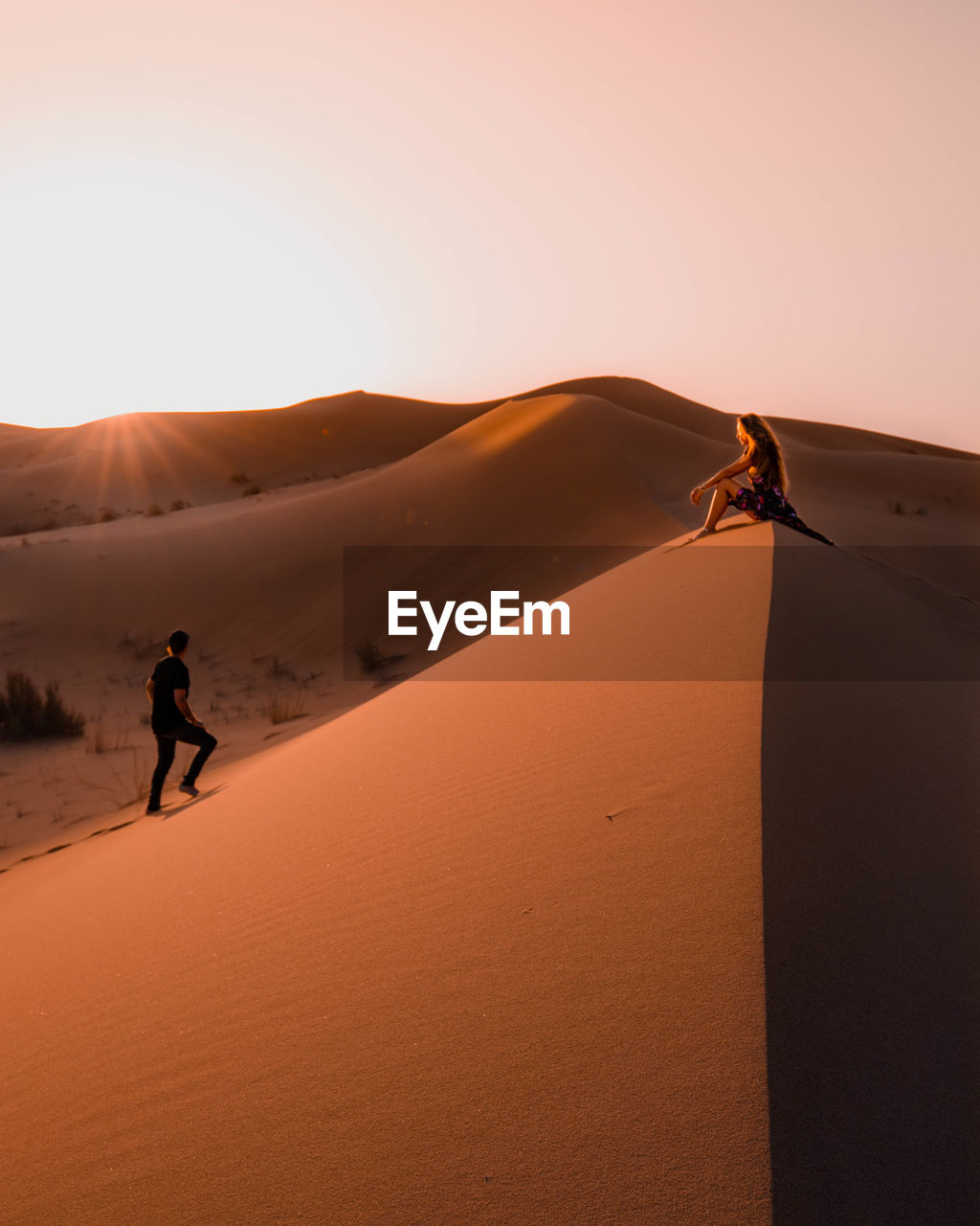 Couple sitting in the sahara desert in morocco during sunset