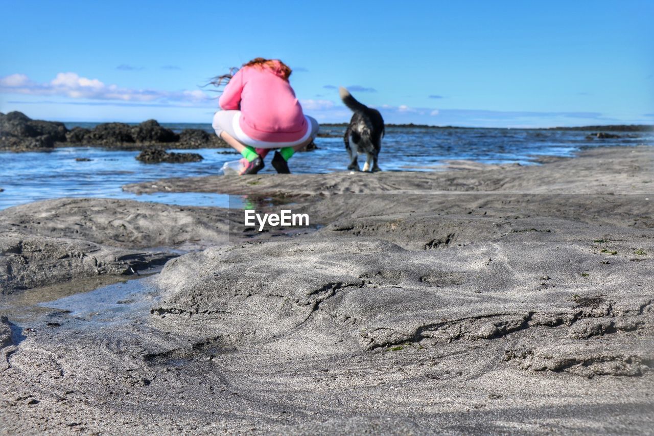 REAR VIEW OF WOMAN WITH DOG ON BEACH AGAINST SEA