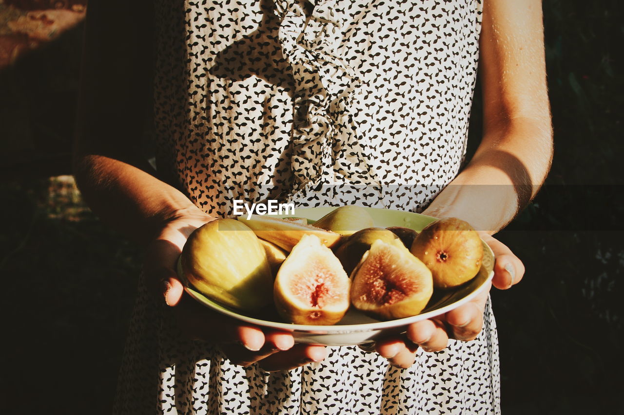 Midsection of woman holding figs on plate during sunny day