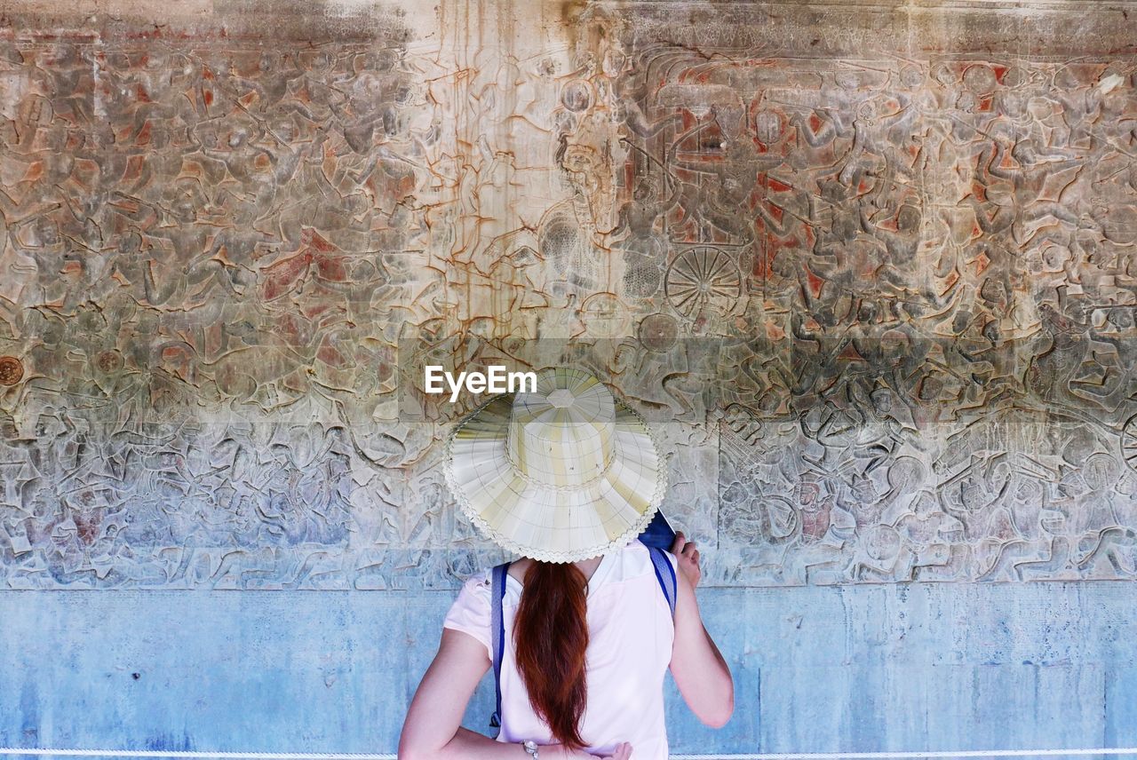 Rear view of woman looking at ancient text on angkor wat wall