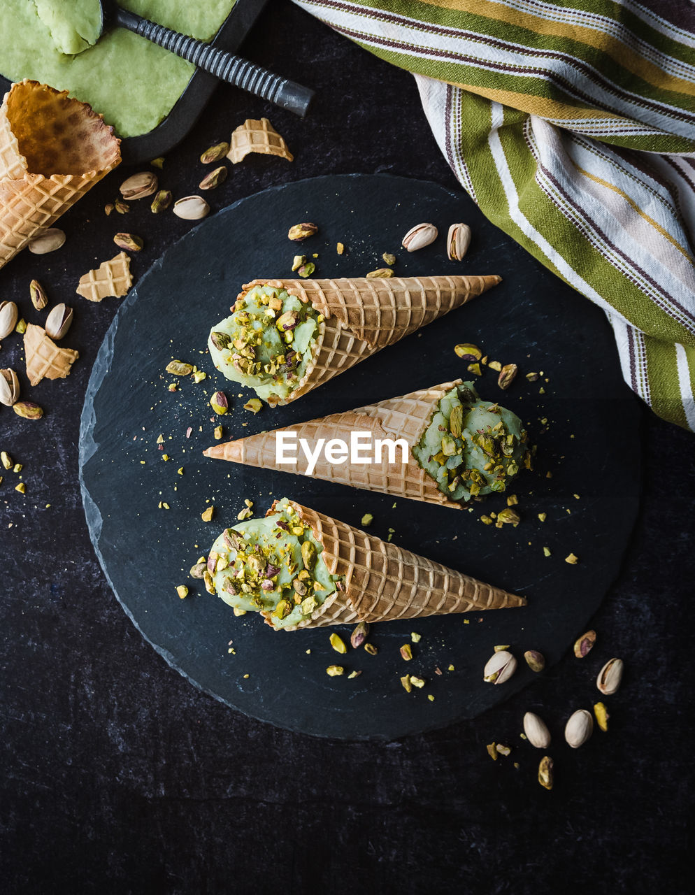 Overhead view of pistachio ice cream in cones on black background.