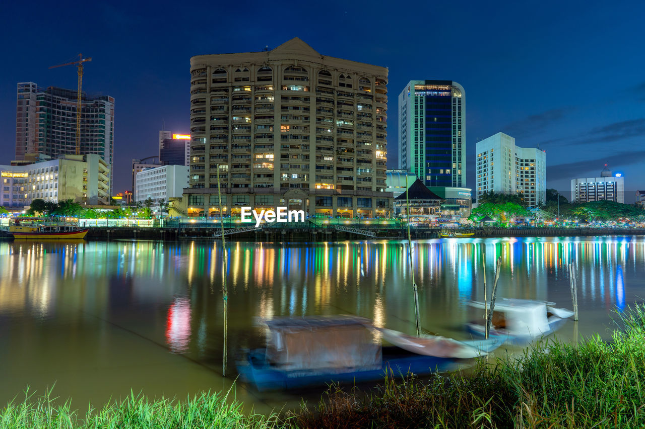 Illuminated buildings by river against sky at night