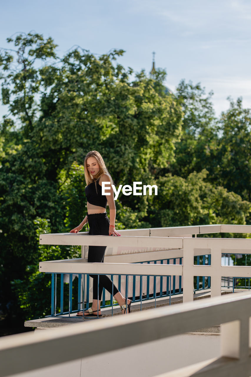 Side view of beautiful young woman standing on balcony against trees