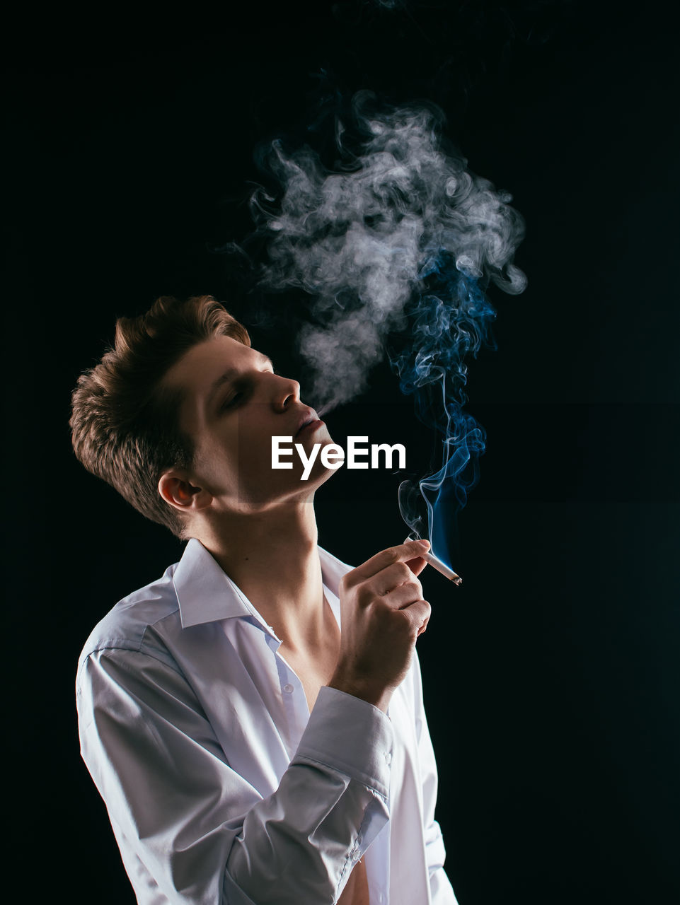 Close-up of man smoking cigarette over black background