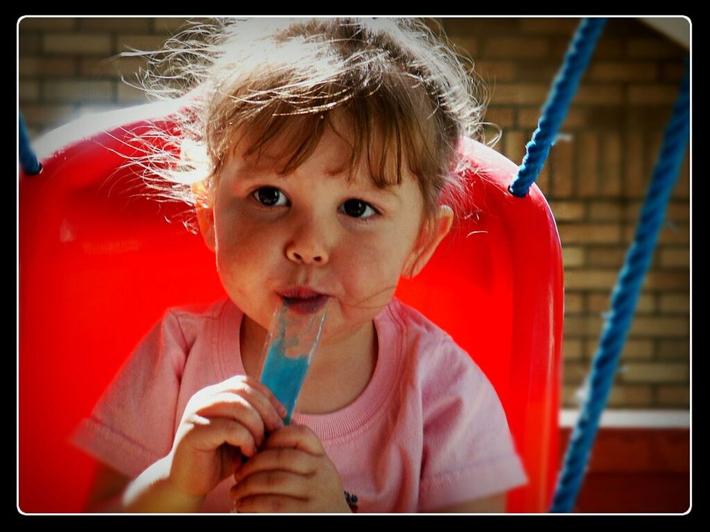 Cute girl eating frozen sweet while sitting on swing outdoors