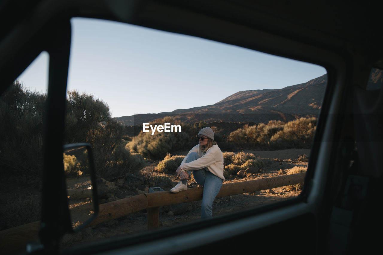 Woman sitting on railing seen through car window