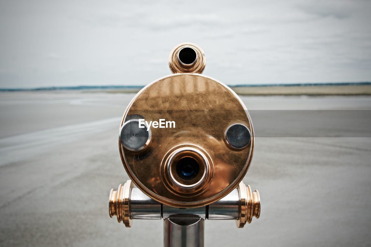 Close-up of coin-operated binoculars at beach against sky