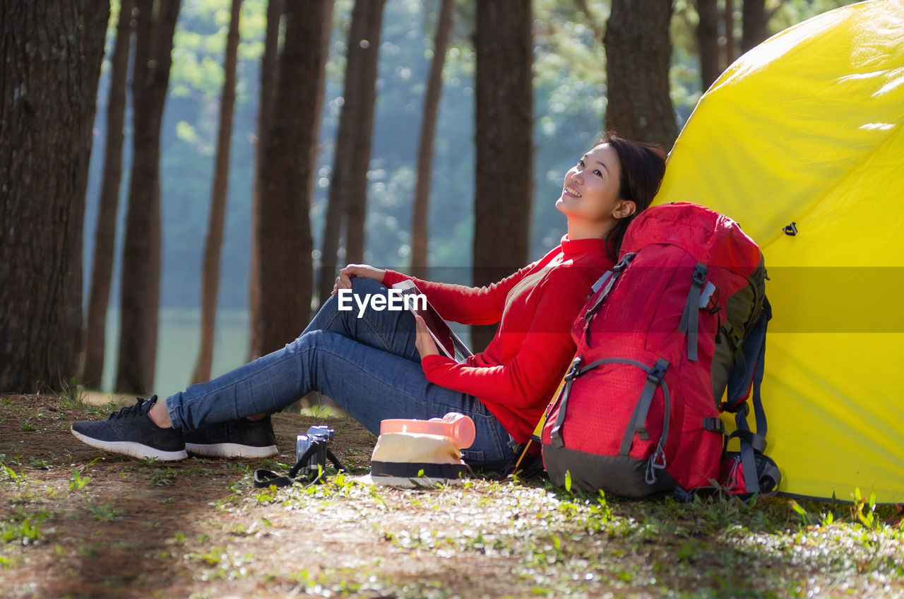 Woman leans against a tent with a backpack, she is use a tablet, pang oung, mae hong son, thailand.