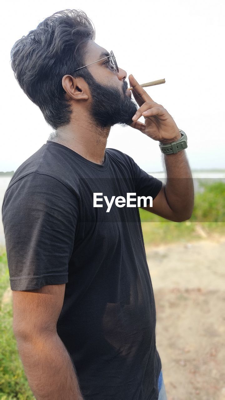 SIDE VIEW OF YOUNG MAN HOLDING CAMERA