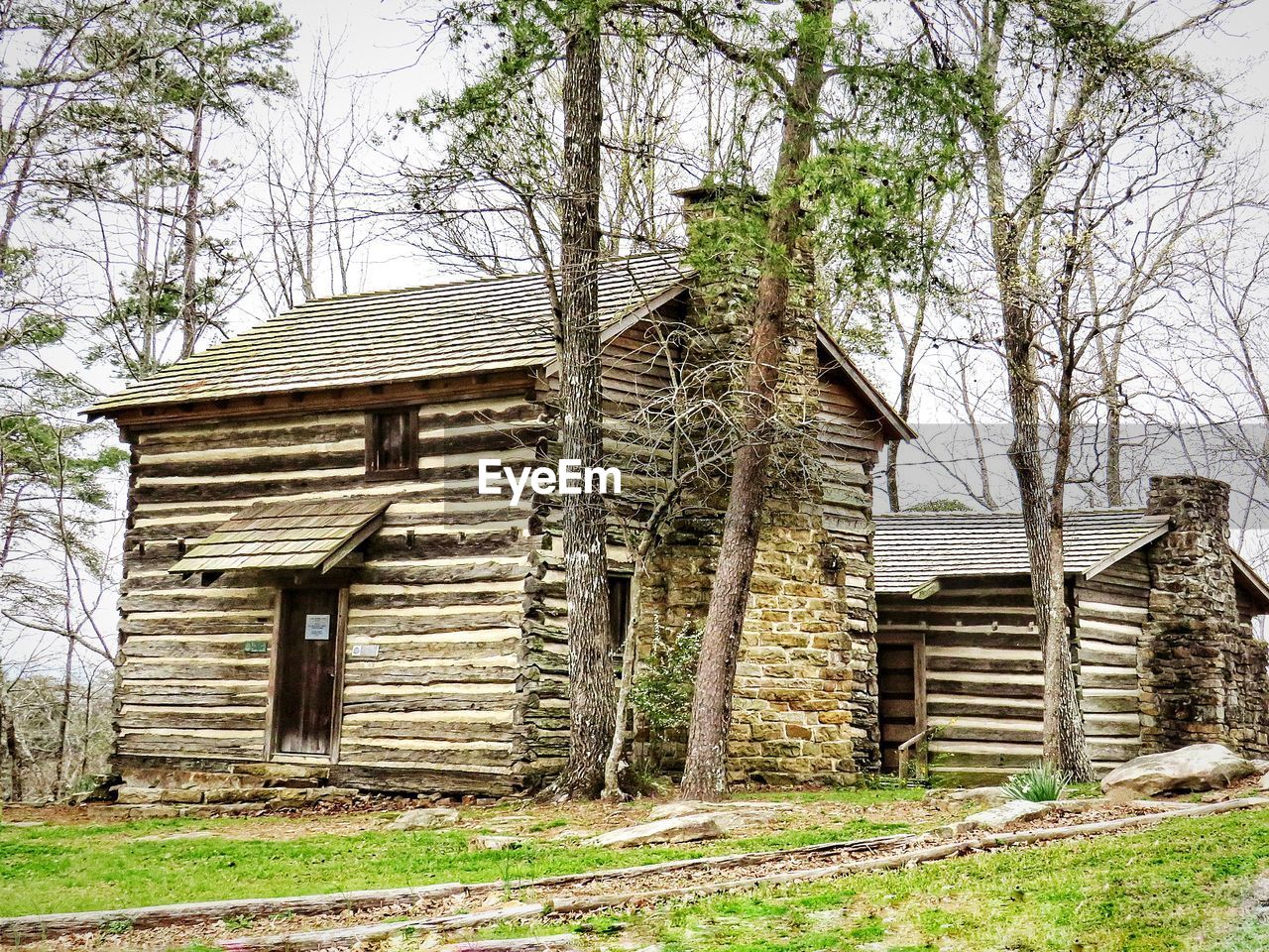 Old wooden house on field by trees against sky