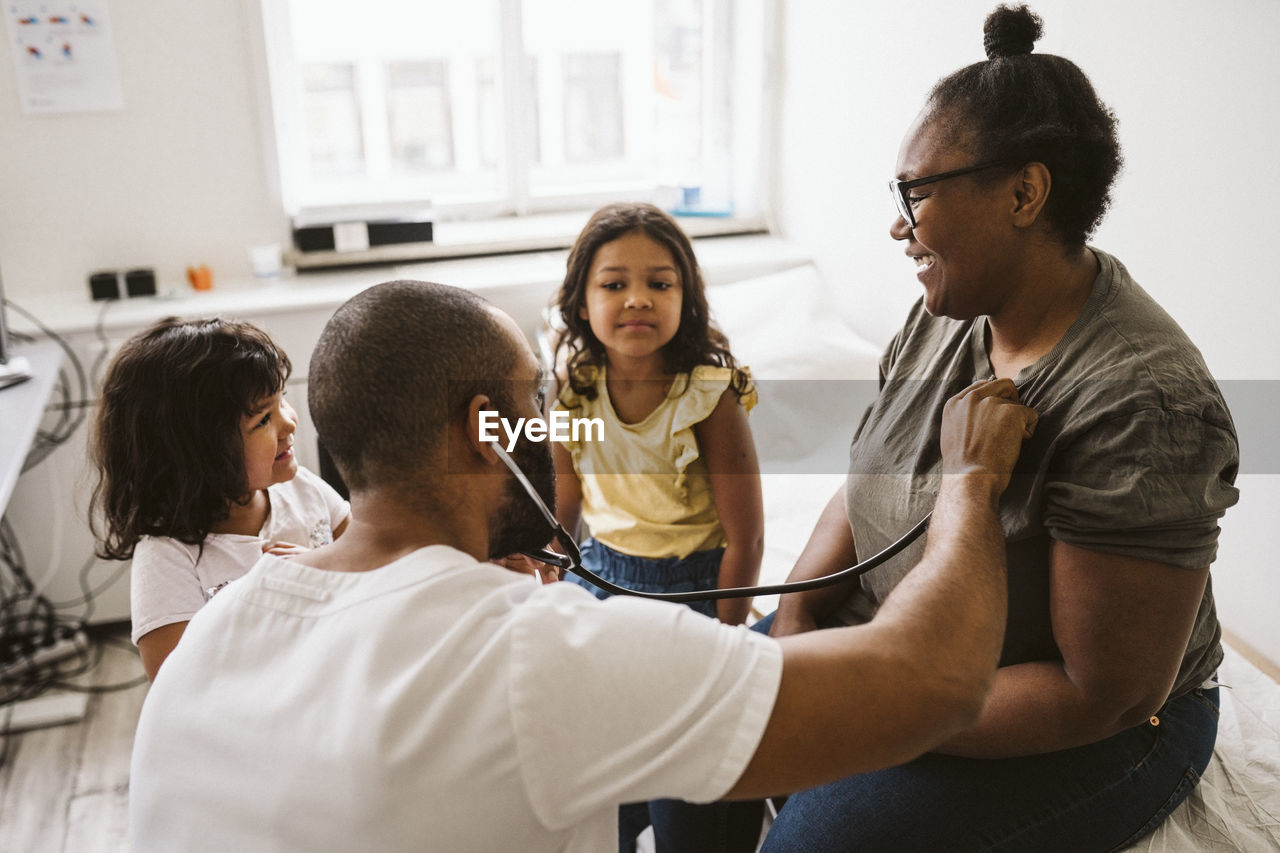 Male healthcare worker with stethoscope examining smiling woman looking at daughter