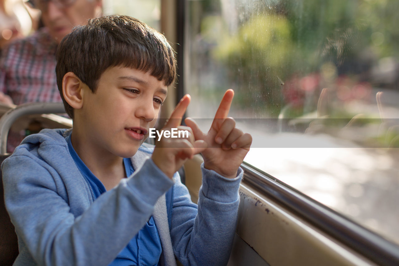 Boy sitting by window while gesturing in tram