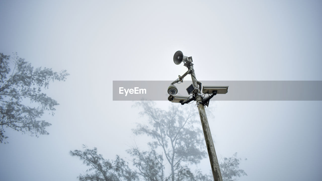 Low angle view of megaphone and security camera against sky during foggy weather