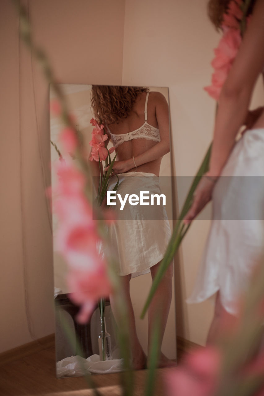 Woman wearing lingerie holding flowers while reflecting on mirror at home