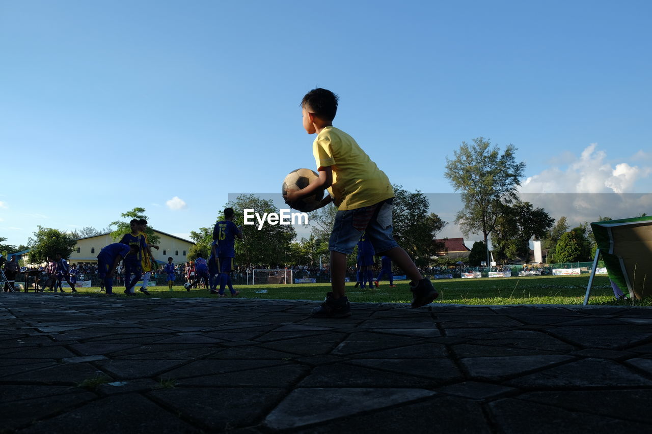 Boy playing soccer on field against sky