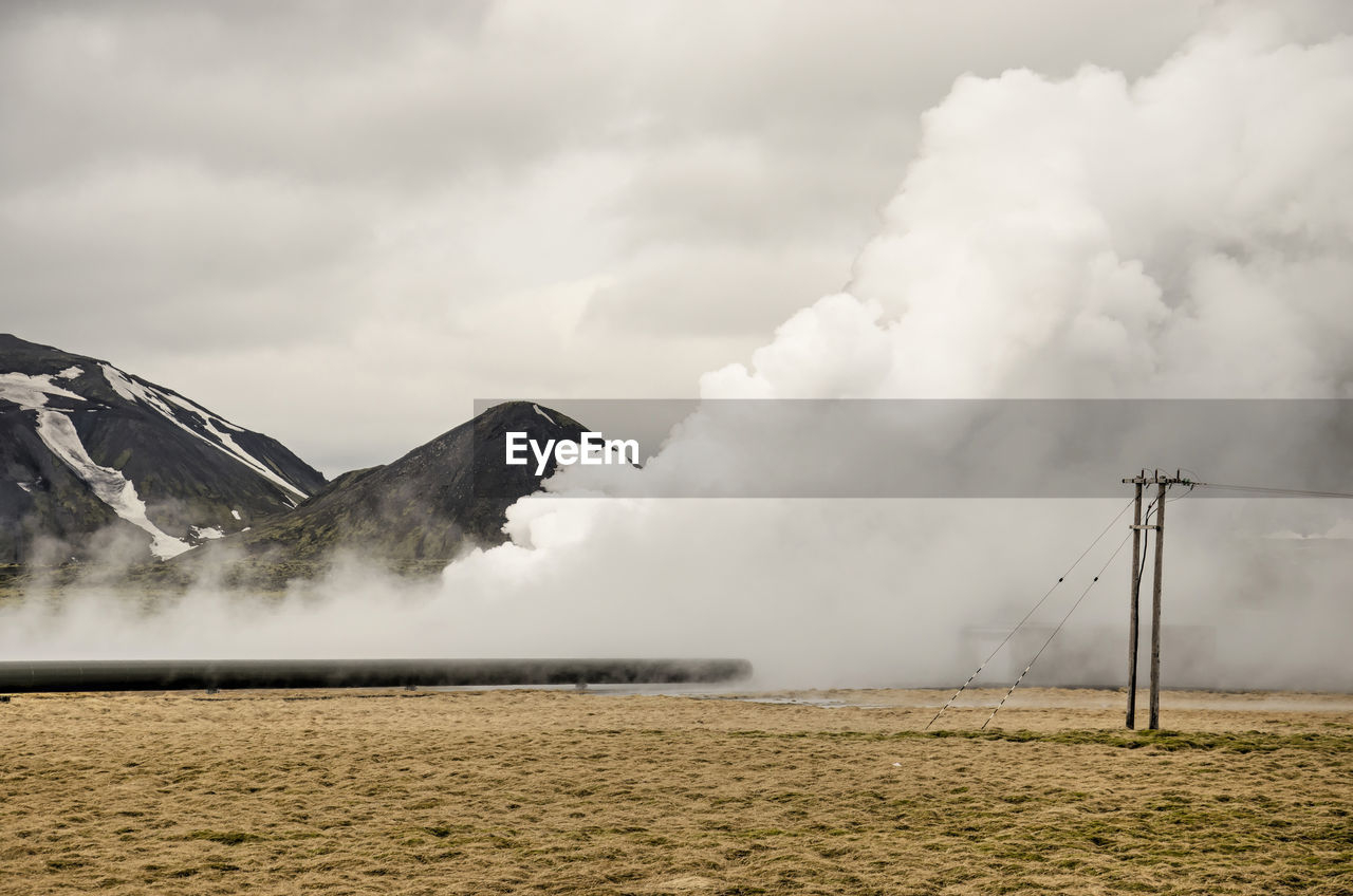 Hot steam coming out of the ground in a grassy landscape with power lines near the  power plant