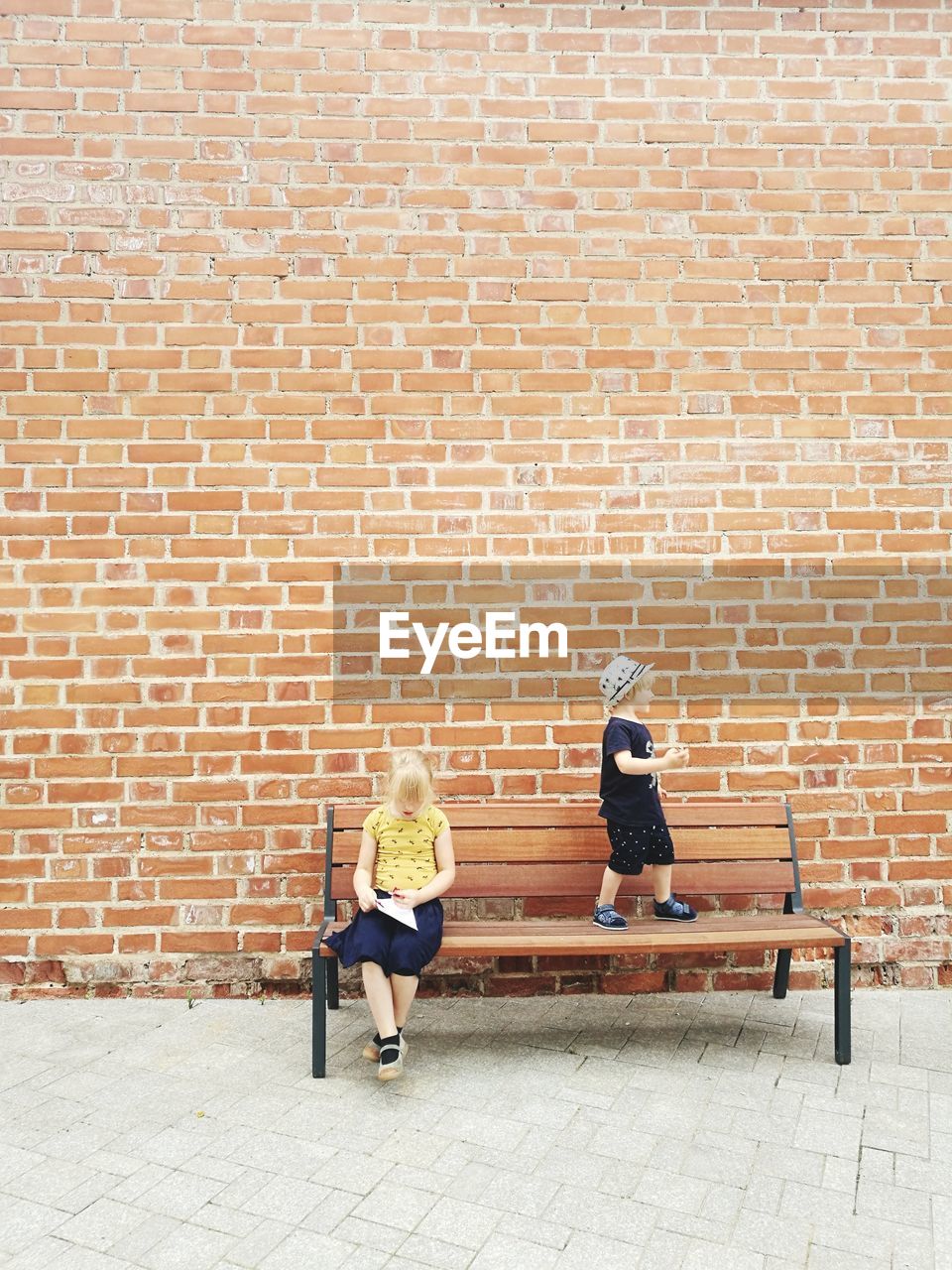 Siblings on bench against brick wall