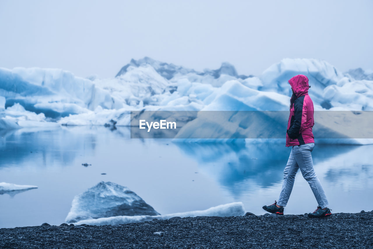 MAN STANDING ON FROZEN LAKE AGAINST SKY