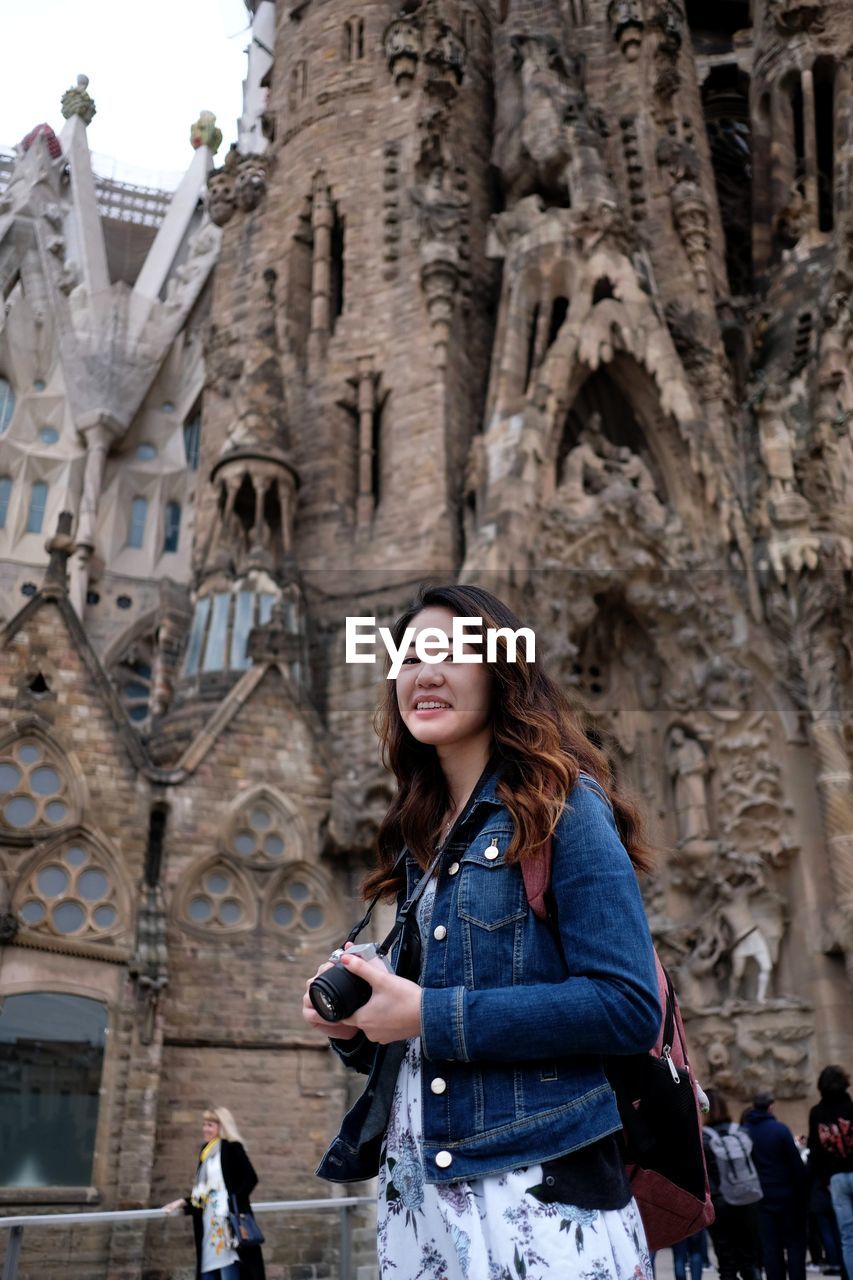 Portrait of smiling young woman standing against building in city