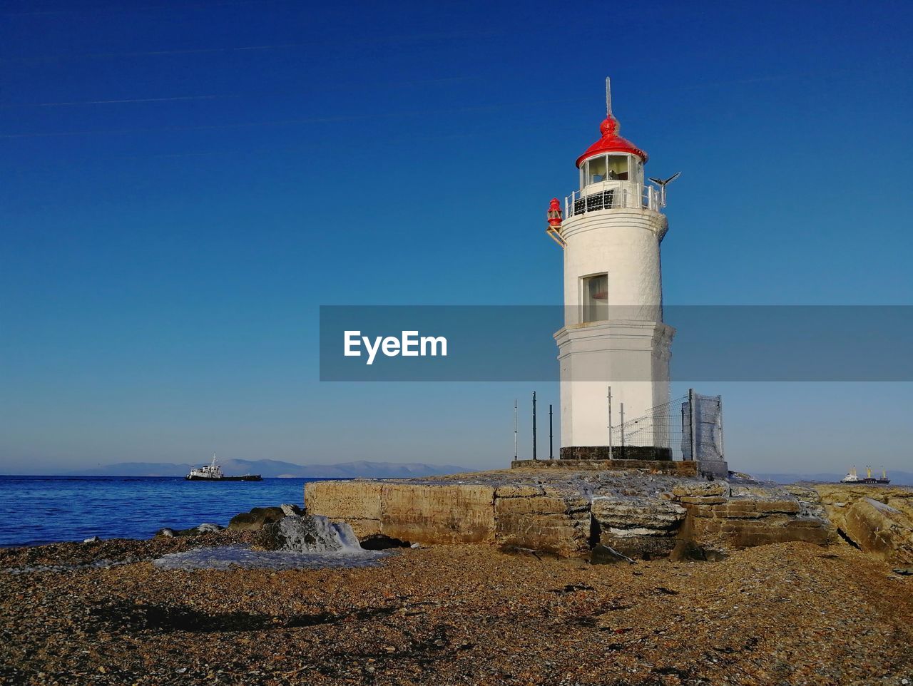 LIGHTHOUSE AMIDST SEA AND BUILDINGS AGAINST SKY