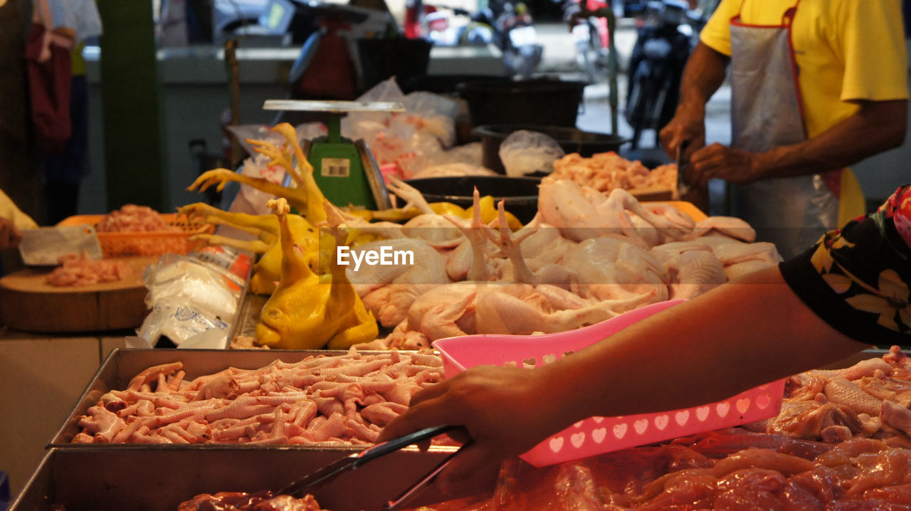 Cropped hand of woman picking meat with tongs in market