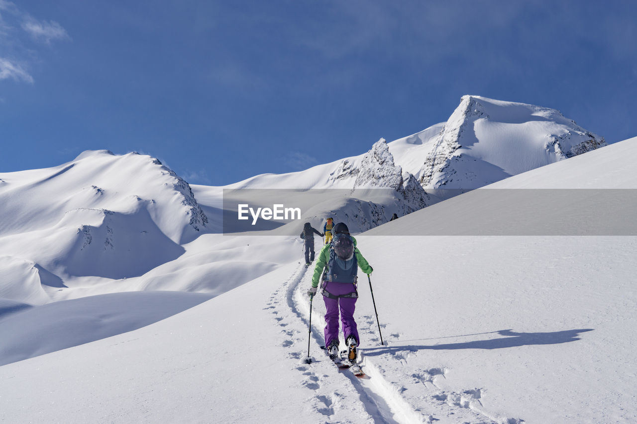 Rear view of people skiing on snowcapped mountain against sky