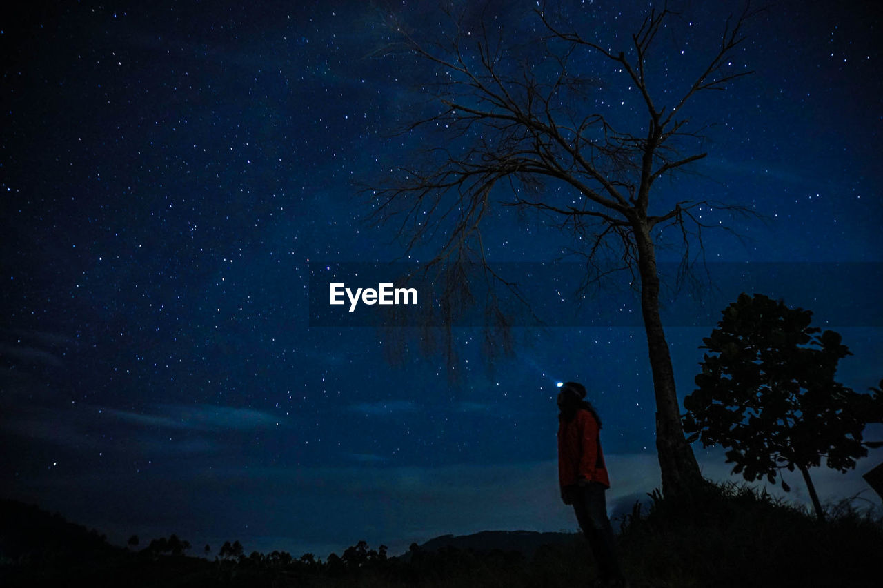 Low angle view of silhouette woman standing on field against starry sky