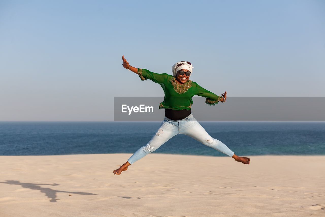 Young woman jumping on beach against clear sky