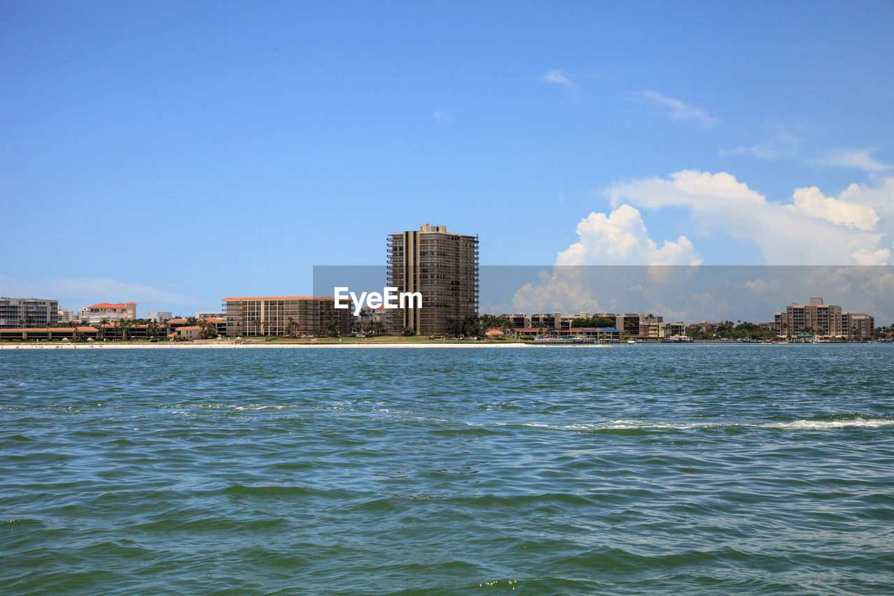 Sea by buildings against blue sky